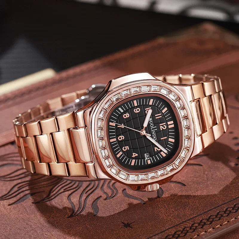 Rose gold wristwatch with black square dial, crystal bezel, and metal link bracelet on leather surface
