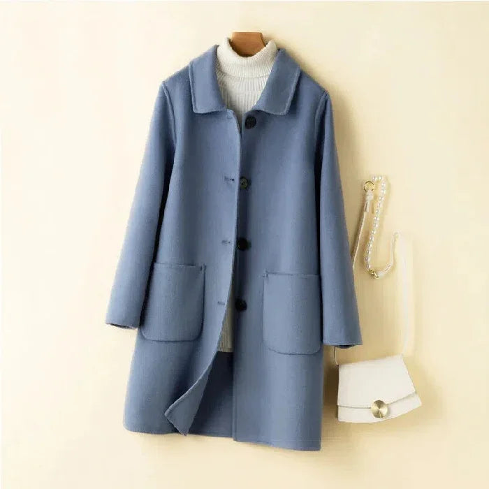 Blue woolen buttoned coat with large pockets on white background, paired with white turtleneck and white handbag