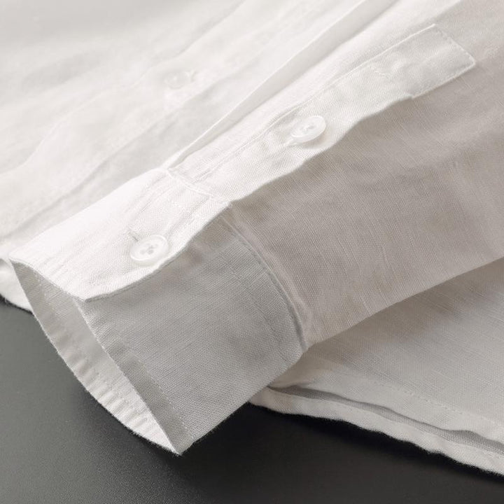 Close-up of white linen shirt cuff with button detailing on black surface