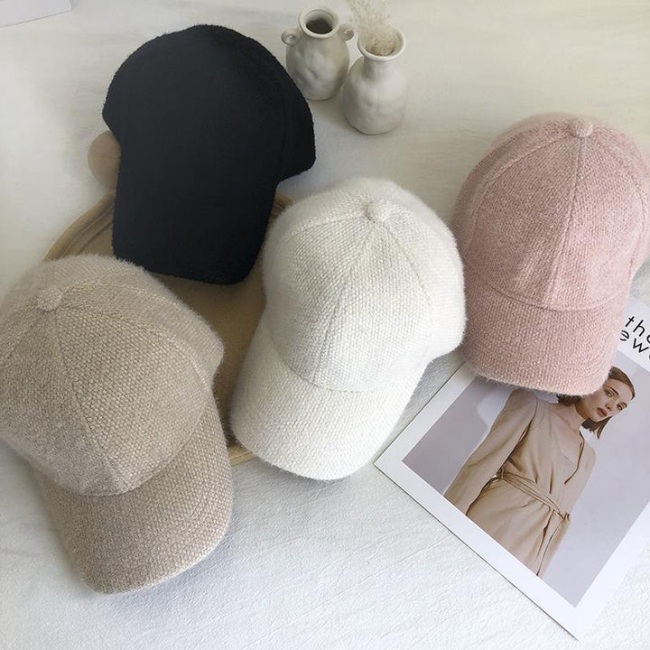 Soft knit baseball caps in beige, black, white, and pink on white fabric with a fashion magazine and decorative vases