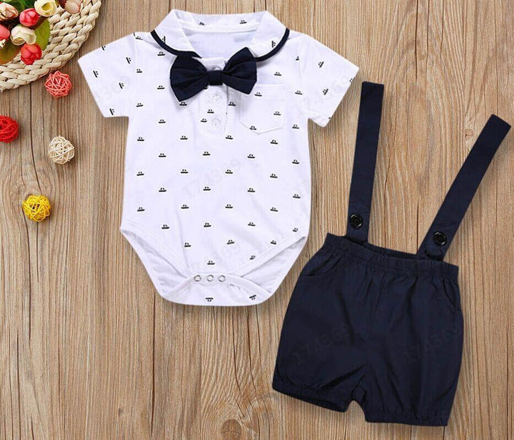baby boy white onesie with black bow tie and printed hats, paired with navy blue suspender shorts on wooden background