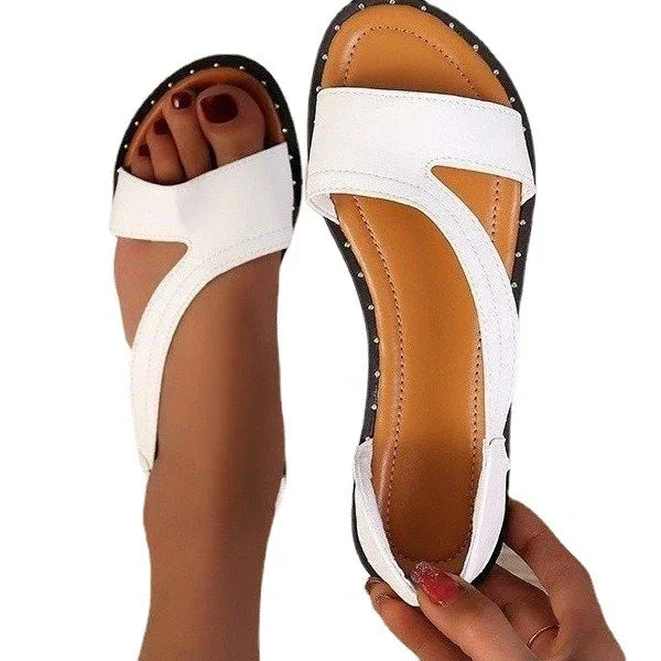 White women's sandals with tan footbeds and studded black soles, one worn and one held in hand
