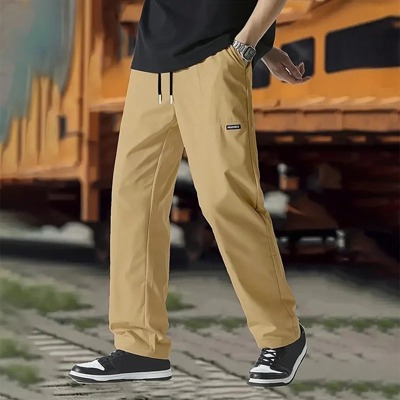 Person wearing beige casual pants with drawstring, black sneakers near industrial yellow train car