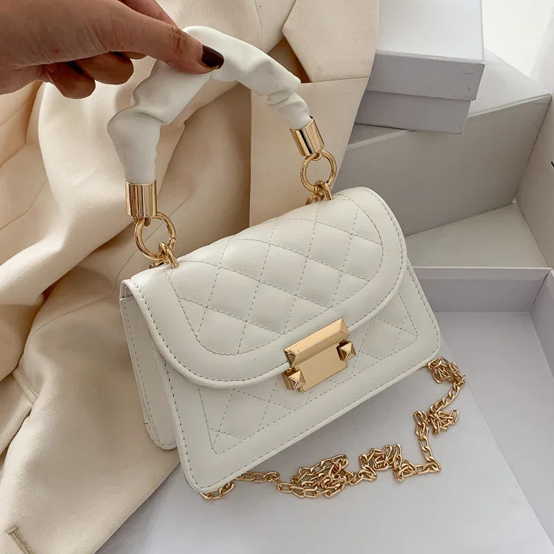 White quilted leather handbag with gold chain strap and padded handle on beige fabric