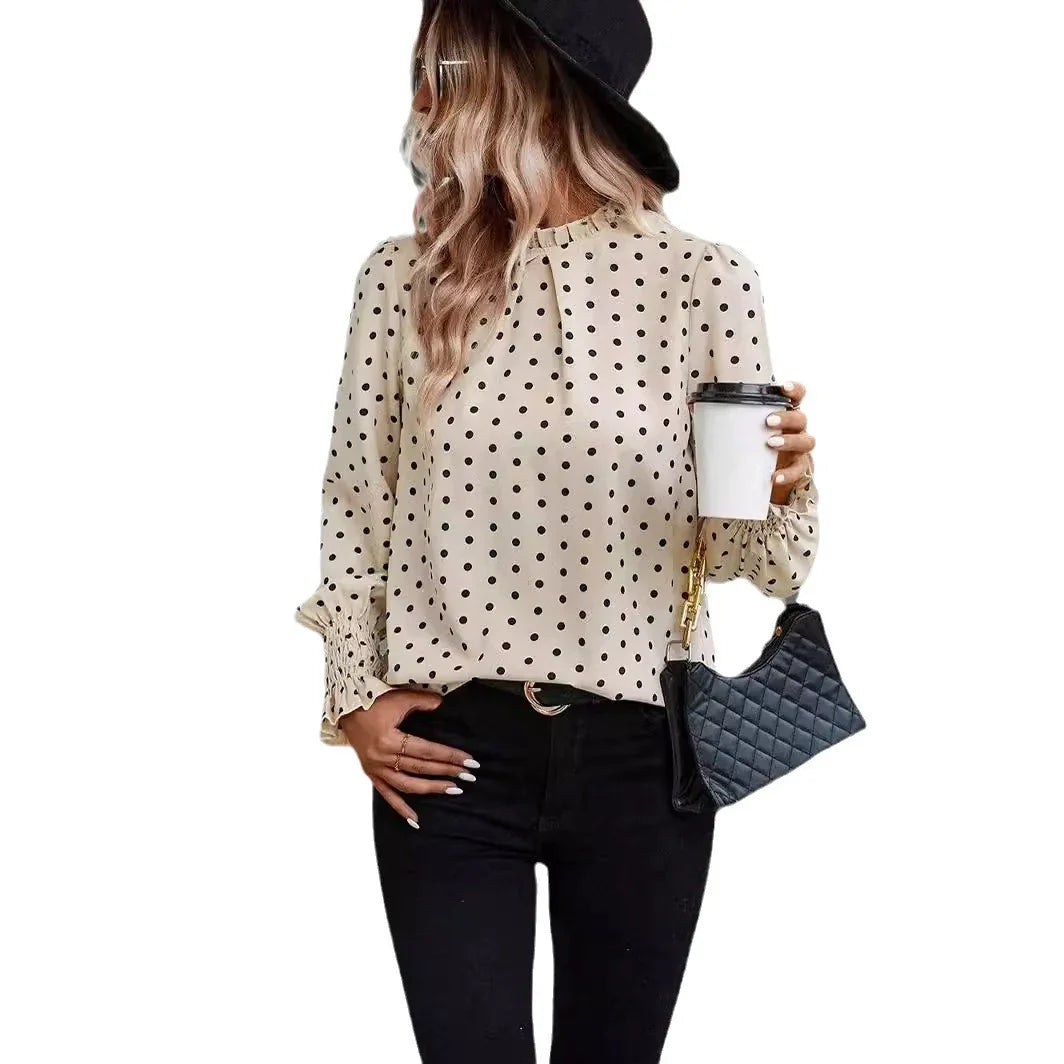 Woman wearing beige polka dot blouse with long sleeves, black jeans, black hat, holding coffee cup and black quilted handbag