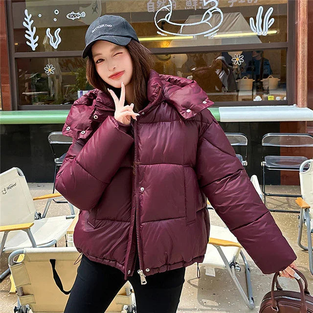 Young woman in a burgundy puffer jacket and black cap posing outdoors at cafe seating area