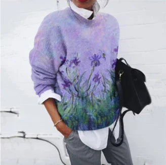 Woman wearing oversized purple floral sweater over white shirt, gray pants, and holding black bag against white wall