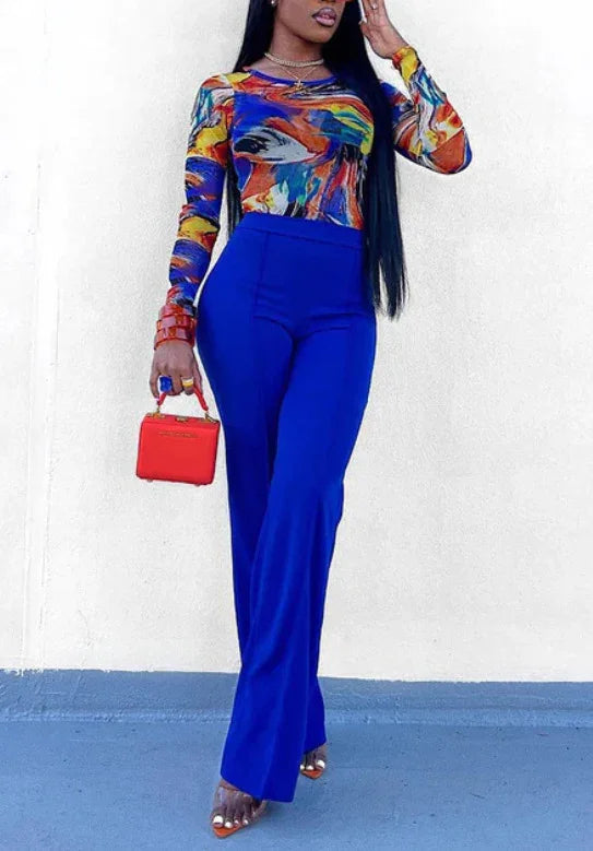 Woman wearing colorful abstract long-sleeve top, cobalt blue pants, holding small red handbag