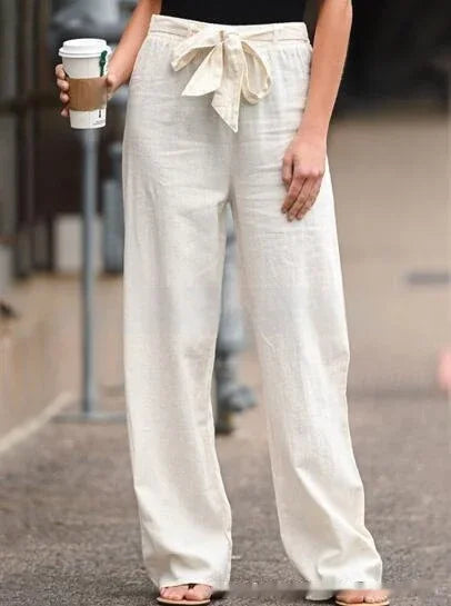 Woman wearing beige linen wide-leg pants with bow tie waist holding coffee cup outdoors