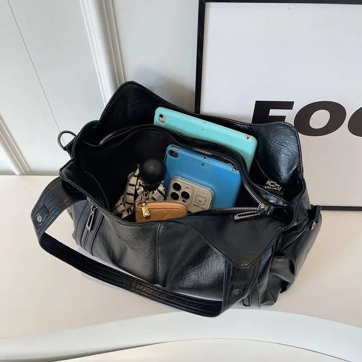 Black leather handbag containing two blue smartphones, a small brown wallet, and a patterned umbrella on a white surface