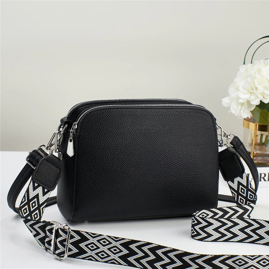Black textured leather crossbody bag with silver zippers and a black and white geometric adjustable strap