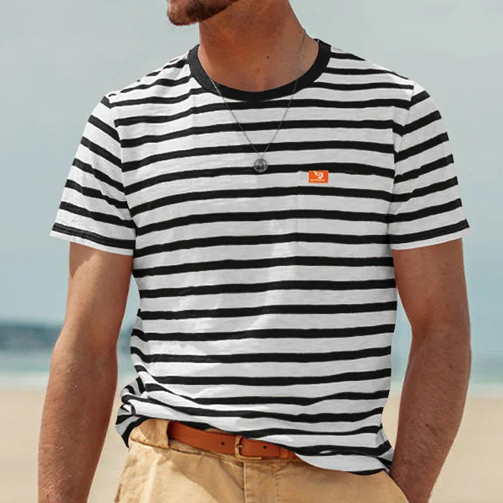 Man wearing a black and white striped T-shirt with a small orange logo on chest at the beach