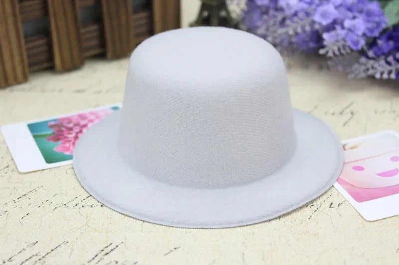Simple light gray felt bowler hat on textured surface with floral cards and purple flowers background