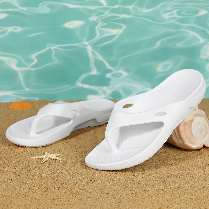 White beach sandals on sand near seashells with turquoise water background