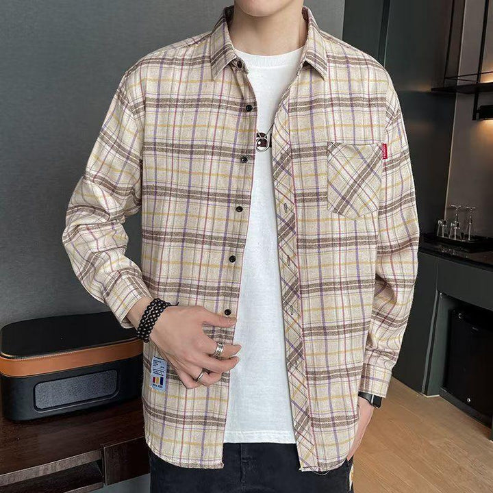 Man wearing beige and brown plaid button-up shirt over white t-shirt with black pants indoors