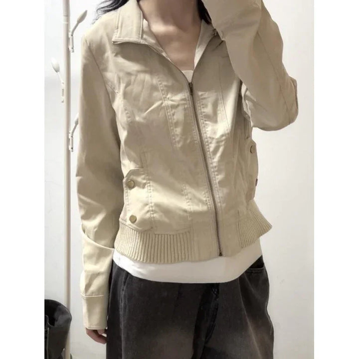 Woman wearing beige zip-up jacket with ribbed hem and button details over white top