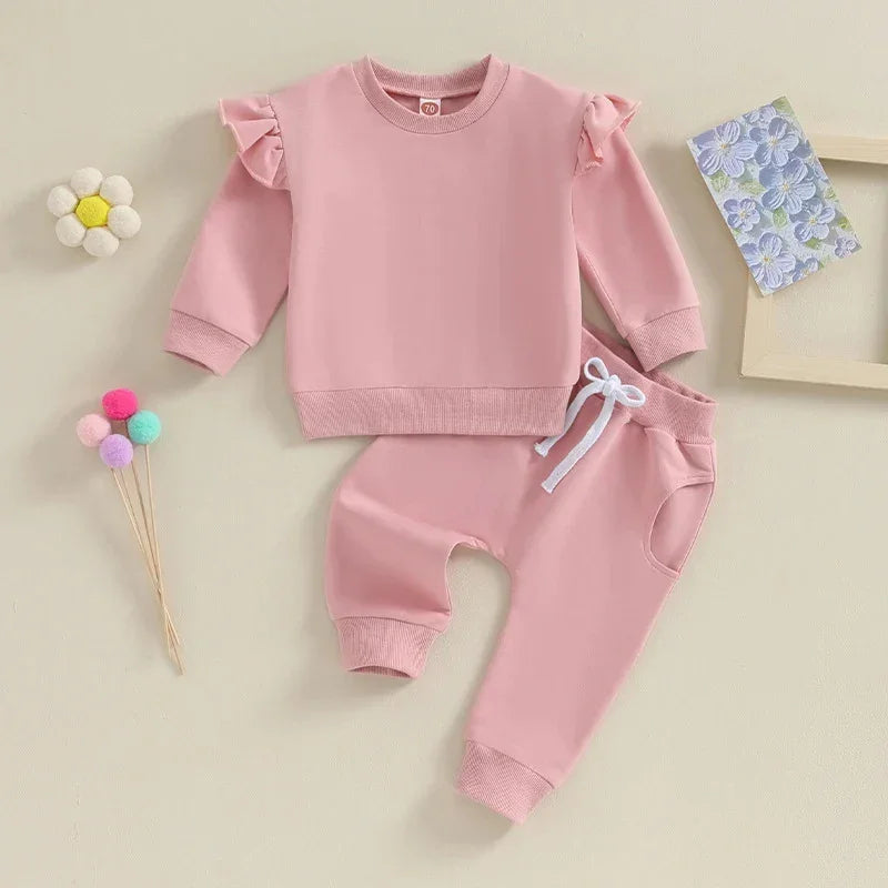 Pink toddler outfit with ruffle shoulder sweatshirt and drawstring pants on beige background
