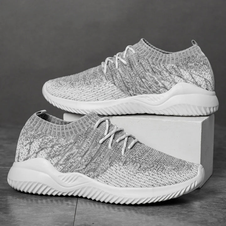 Pair of gray knit athletic sneakers with white soles on gray background and white block
