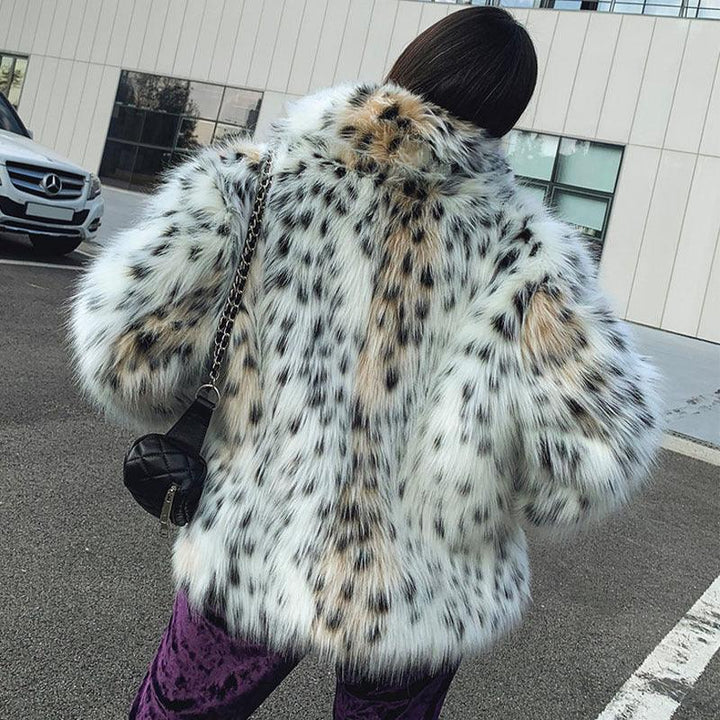 Person wearing white and black spotted faux fur coat with leopard print pattern, standing outdoors near a parked white Mercedes