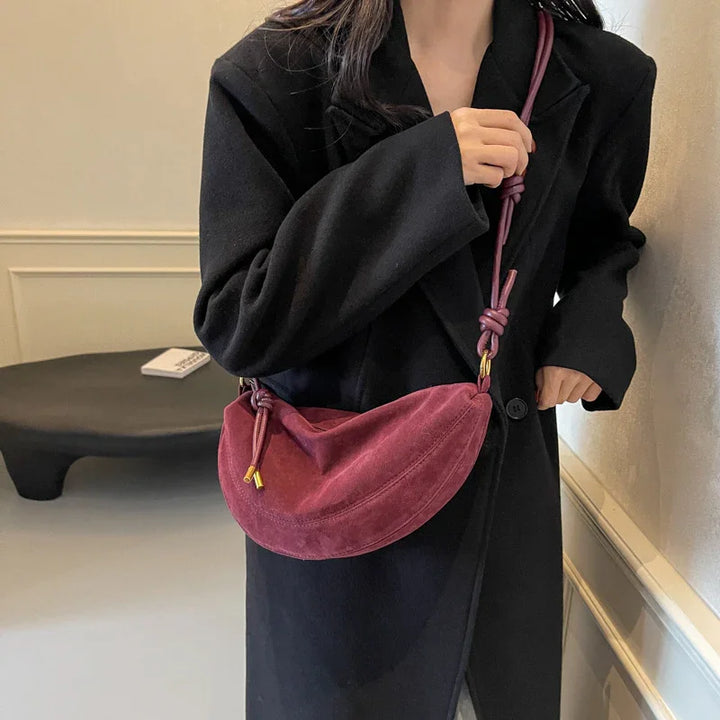 Woman in black coat holding a stylish burgundy suede shoulder bag with knotted strap