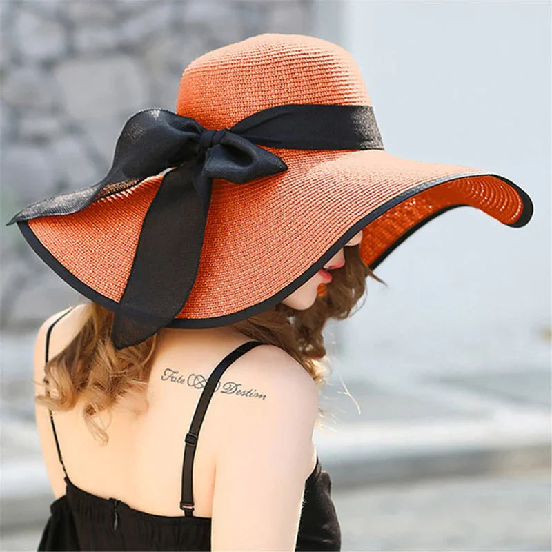 Woman wearing a wide-brimmed orange sun hat with black ribbon, black dress, showing shoulder tattoo