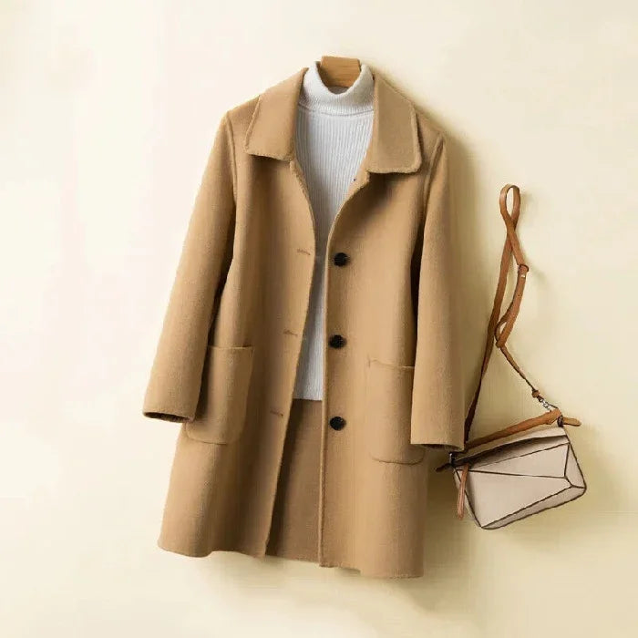 Beige wool coat with black buttons and patch pockets over white turtleneck sweater, paired with beige crossbody bag