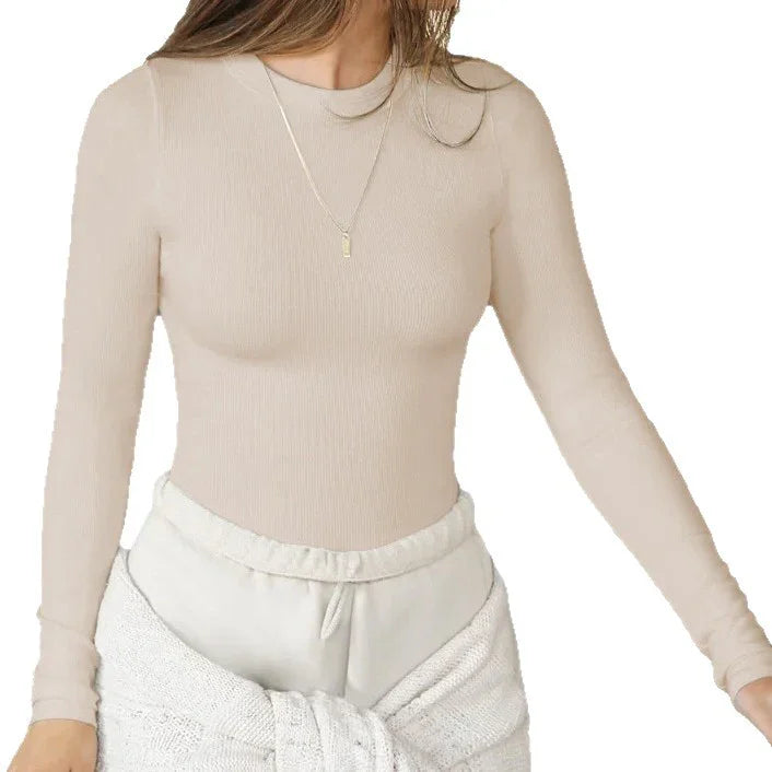 Woman wearing beige ribbed long-sleeve top, white pants, and knit sweater tied around waist