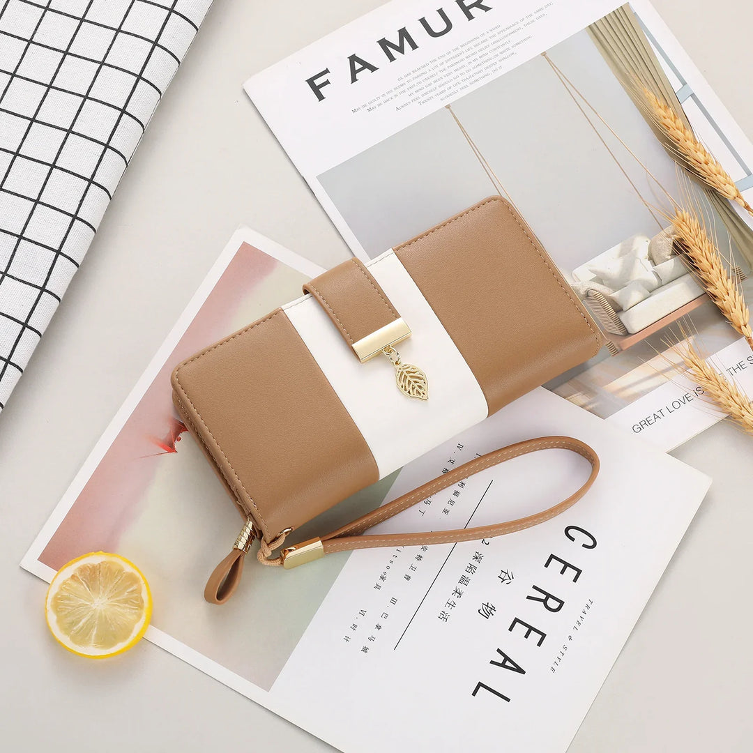 Tan and white leather wristlet wallet with a gold leaf charm, placed on magazines with a lemon slice and wheat stalks