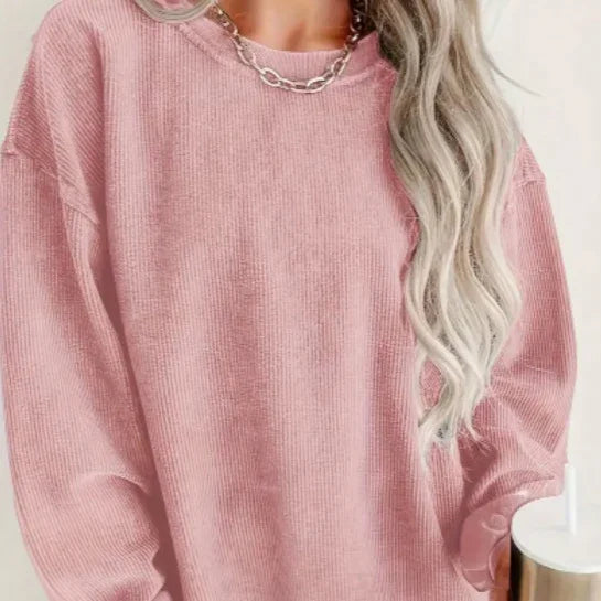 Woman wearing a soft pink ribbed sweater with long blonde wavy hair and a silver chain necklace