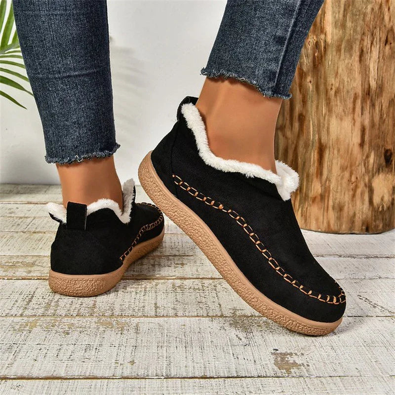 Black slip-on winter shoes with white fur lining and brown stitched sole worn with dark denim jeans