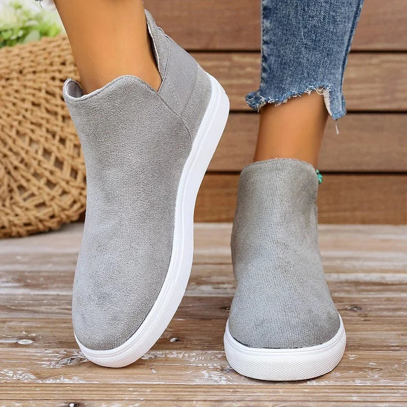 Woman wearing casual grey suede slip-on sneakers with white soles on wooden floor