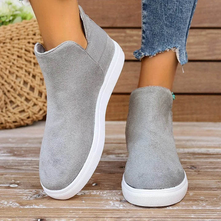 Woman wearing casual grey suede slip-on sneakers with white soles on wooden floor
