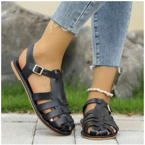 Person wearing black leather gladiator sandals and light blue ripped jeans outdoors on pavement