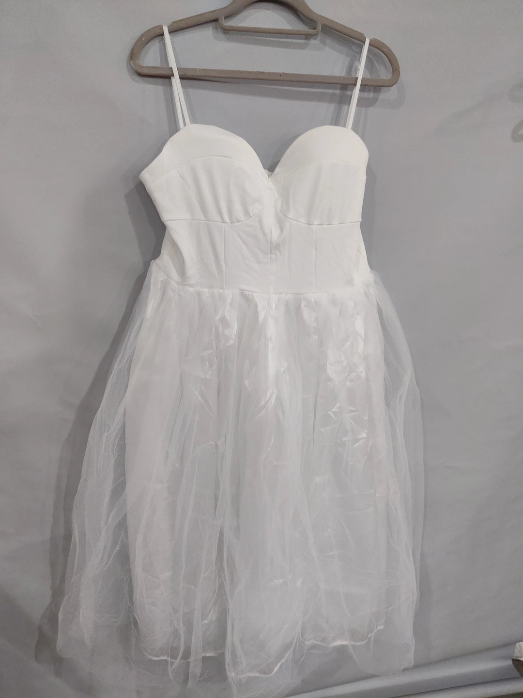White sleeveless dress with fitted bodice and tulle skirt hanging on beige hanger