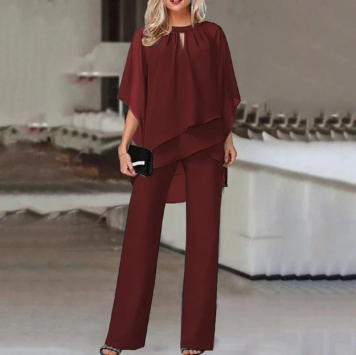 Woman wearing elegant burgundy layered pantsuit with loose top and wide-leg trousers, holding black clutch