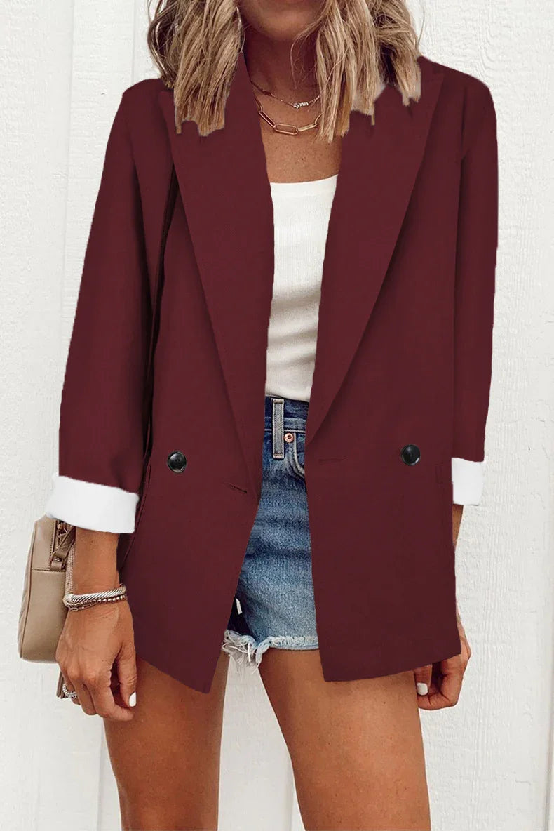 Woman wearing burgundy blazer with white cuffs, white top, denim shorts, and gold necklace