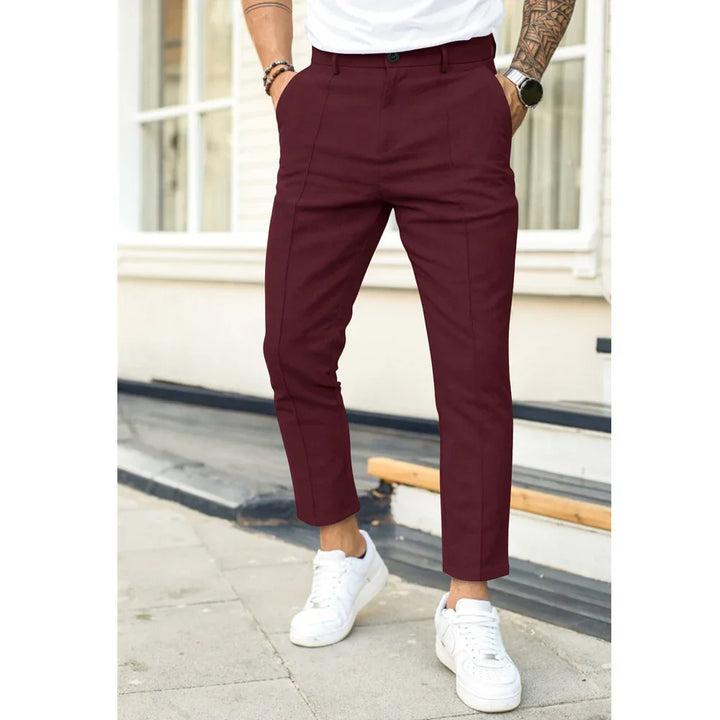 Man wearing slim fit maroon pants and white sneakers standing on city sidewalk