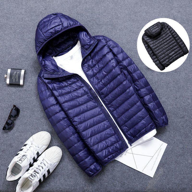 Navy blue lightweight hooded puffer jacket displayed with white sneakers, sunglasses, and a flask on gray surface