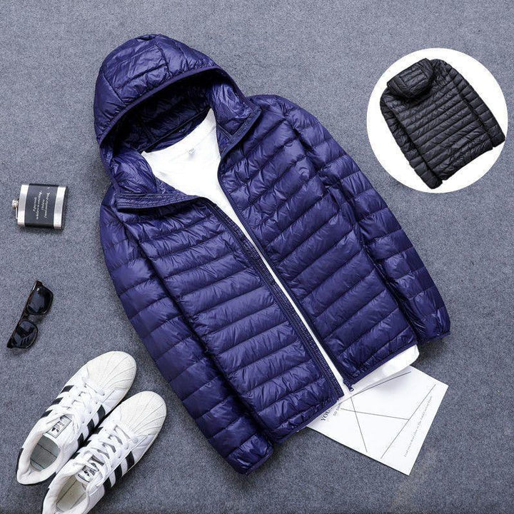 Navy blue lightweight hooded puffer jacket displayed with white sneakers, sunglasses, and a flask on gray surface