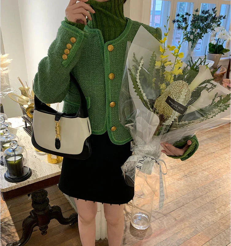 Person in green knit jacket and black skirt holding bouquet and white-black handbag indoors