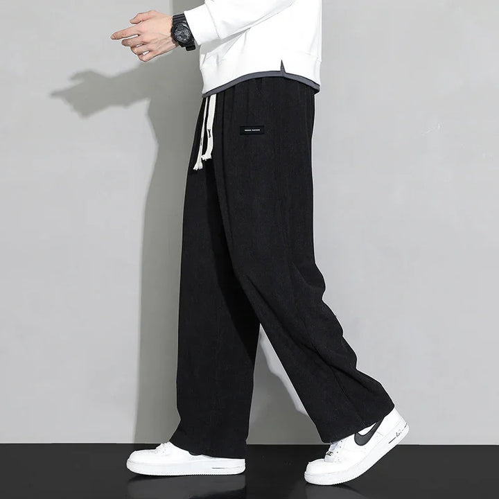 Person wearing black wide-leg pants with white drawstrings and white Nike sneakers, gray background