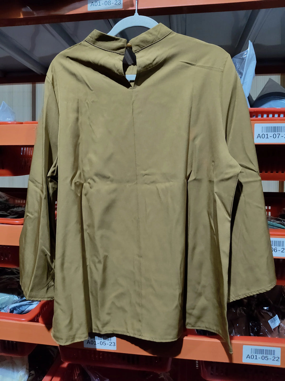 Brown long-sleeve shirt with a buttoned keyhole back hanging on white hanger in warehouse