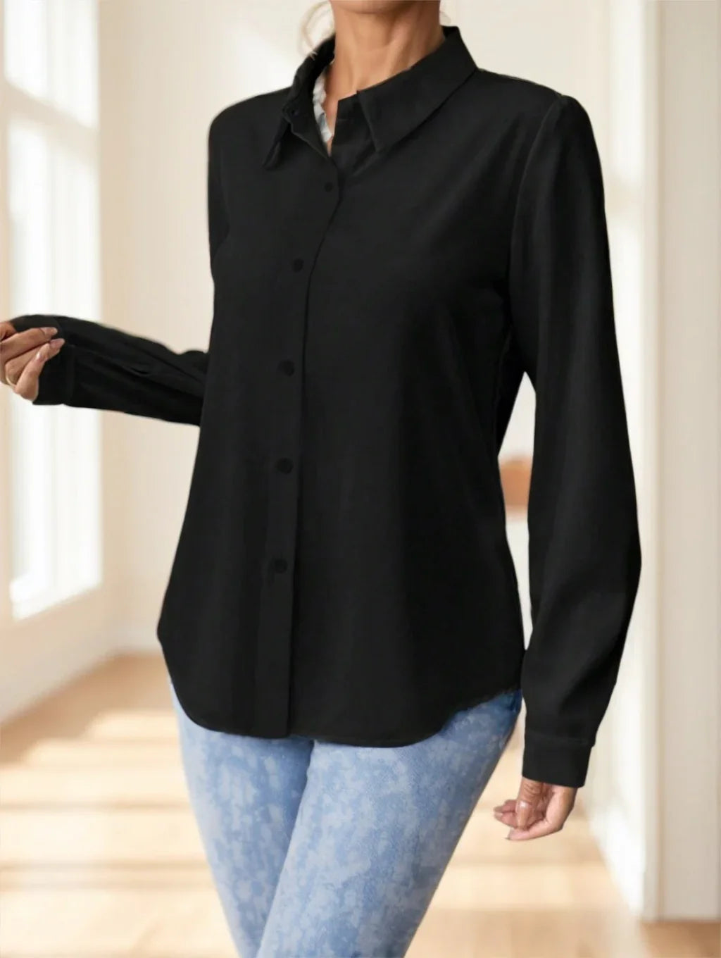 Woman wearing black button-up long sleeve shirt and light blue patterned jeans indoors