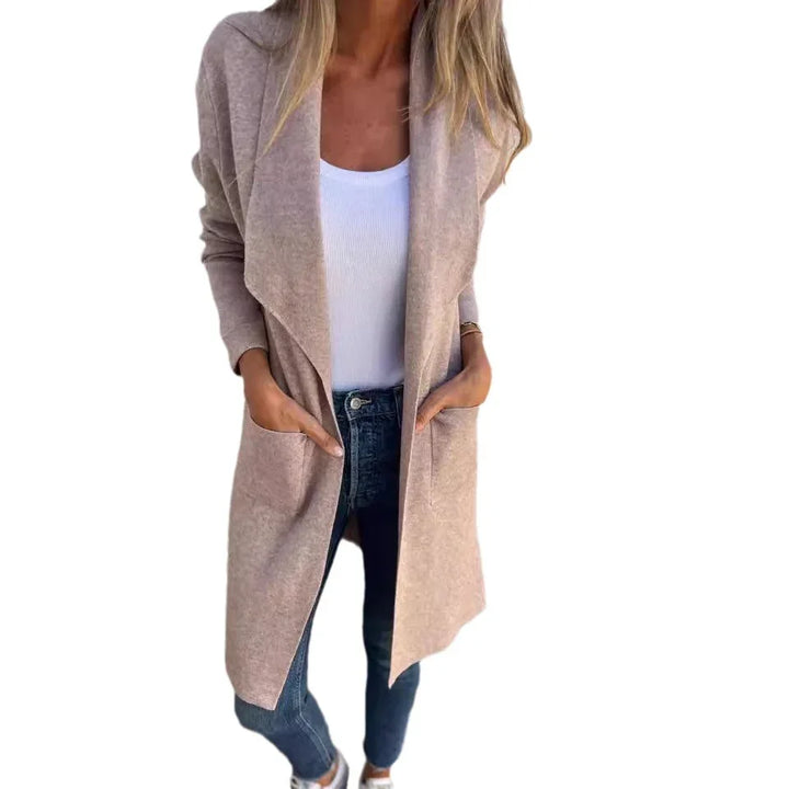 Woman wearing beige open-front cardigan, white tank top, blue jeans, hands in pockets, casual outfit