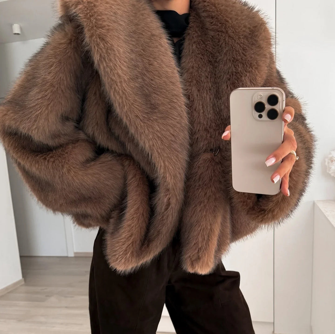 Close-up of person wearing a brown faux fur coat holding a smartphone, indoor modern setting