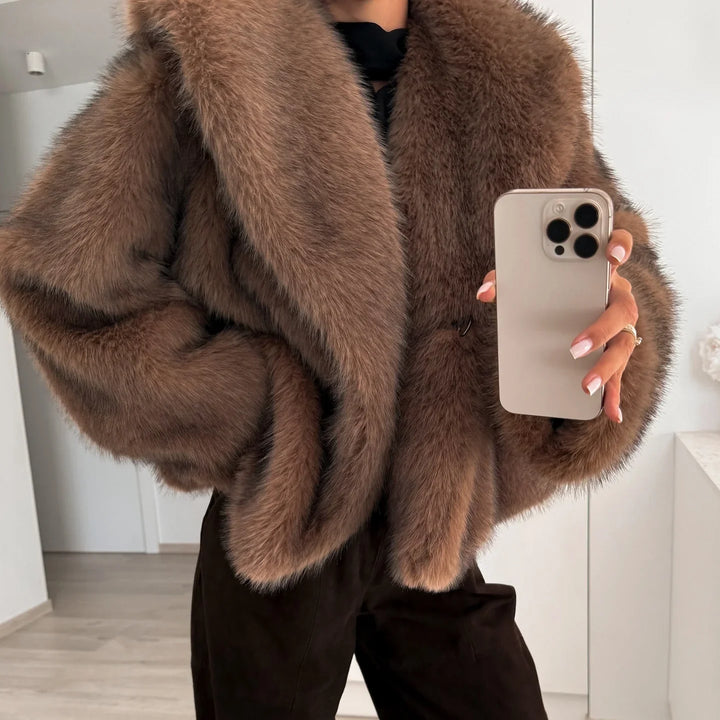 Close-up of person wearing a brown faux fur coat holding a smartphone, indoor modern setting