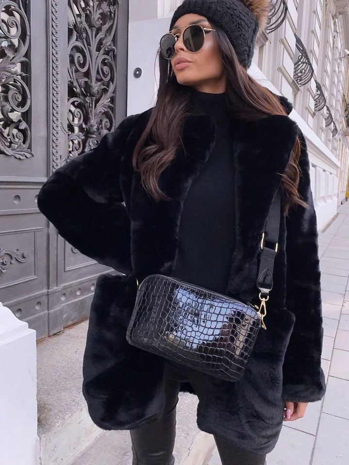 Woman wearing black faux fur coat, black turtleneck, knit beanie with pompom, sunglasses, and black croc-embossed crossbody bag outdoors
