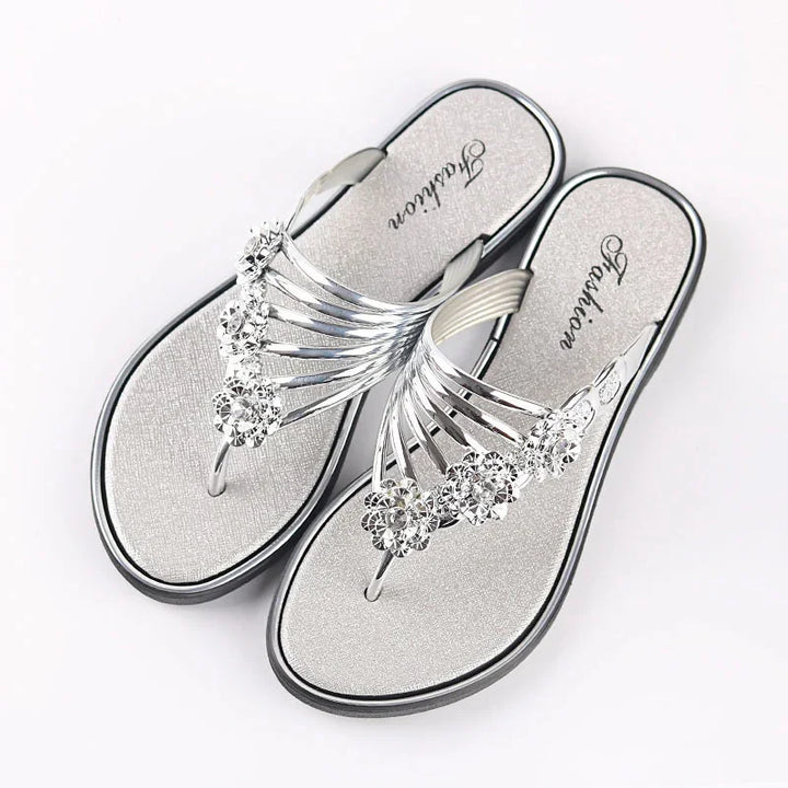 Silver women's flat sandals with rhinestone flower embellishments on white background