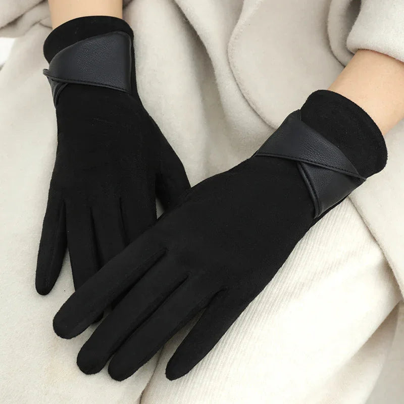 Black winter gloves with leather strap detail worn on hands against beige fabric background