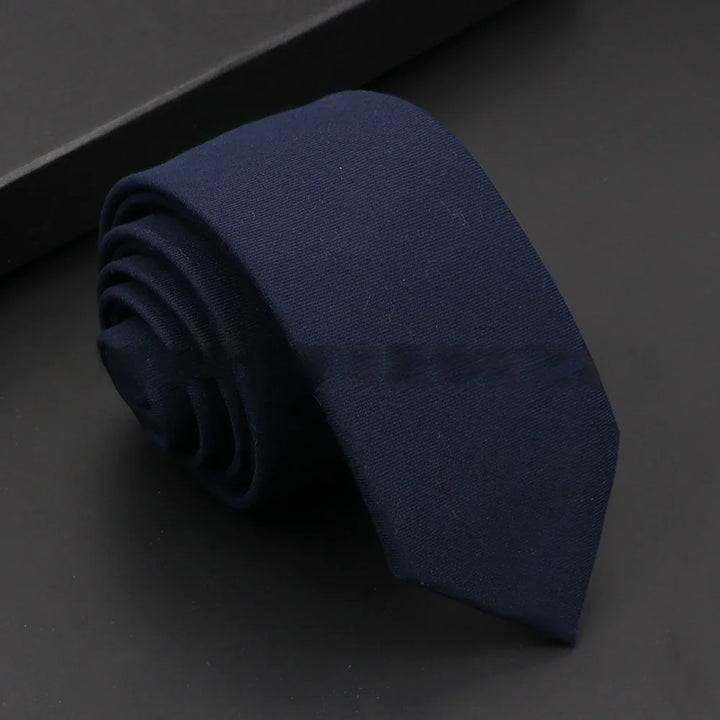 Rolled navy blue men's necktie on black surface with subtle texture